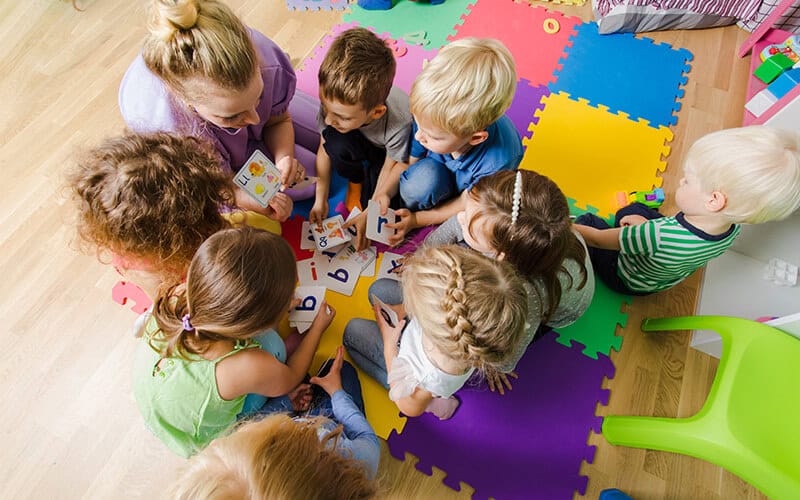 Brightly colored foam mats and ABC flashcards with children and caregiver.