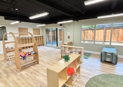 Modern childcare room with large windows, light wood floors, and educational toys for early childhood development.