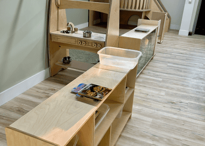 Bright indoor play area featuring a wooden playhouse, kitchen set, and storage for young children.