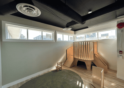 Child-friendly indoor play space with wooden slides, a small chair, and large windows bringing in natural light.