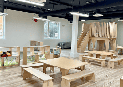 Child-friendly indoor space with wooden benches, tables, climbing structure, and natural light for optimal learning and play.